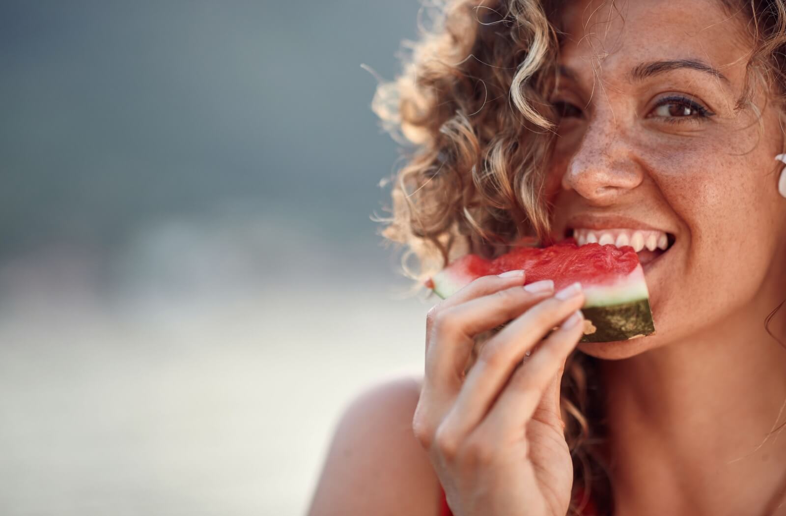 A woman with dental implants biting into a watermelon