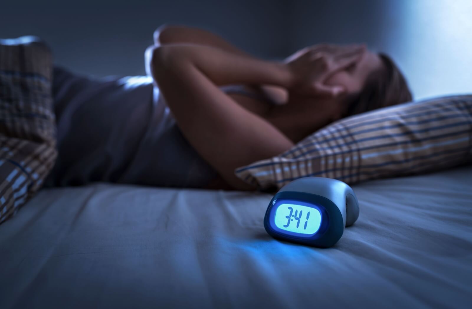 A person lies in bed, frustrated, with a clock showing 3:41 AM, indicating sleep disruption.