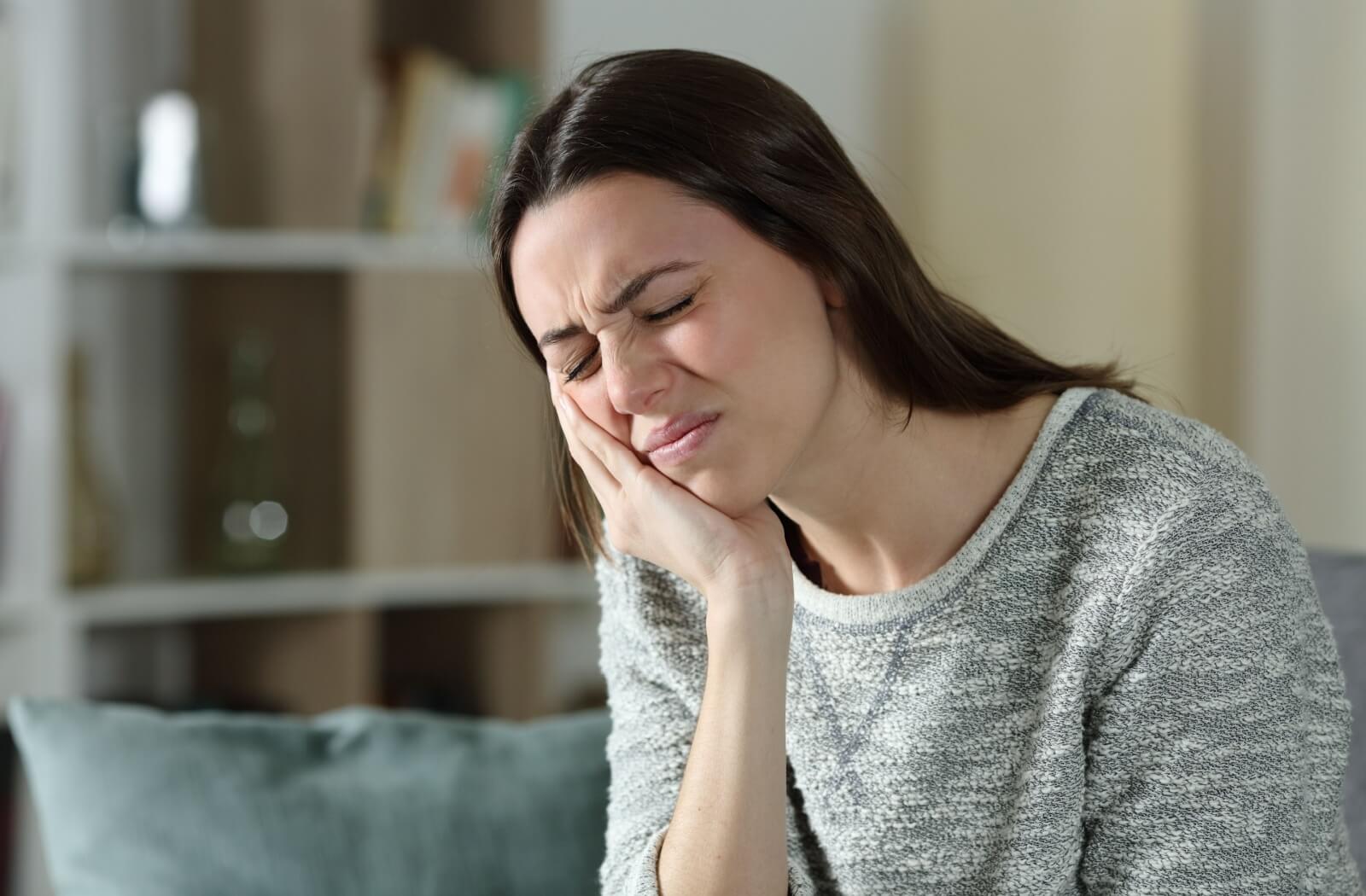 A woman holds her face in pain, possibly from TMJ or sleep apnea-related discomfort.