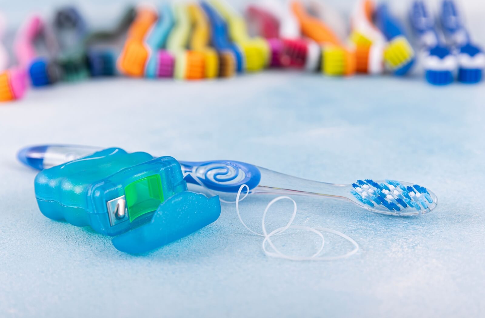 A close-up photo of dental-floss and a toothbrush, with several other toothbrushes in the lined up in the background.