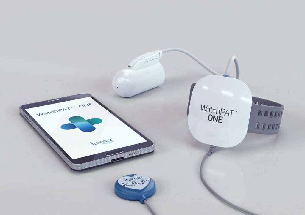 a WatchPAT one sleep apnea take home test sitting on a white surface, showing the watch, finger monitor, and phone app.