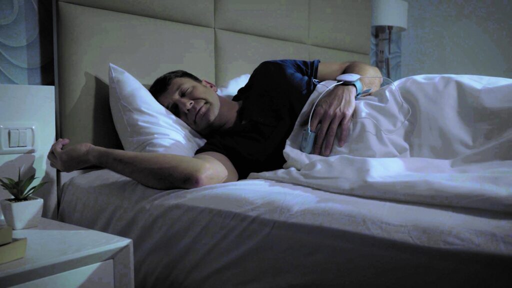 A man sleeping wearing a WatchPAT one sleep apnea take home test watch.