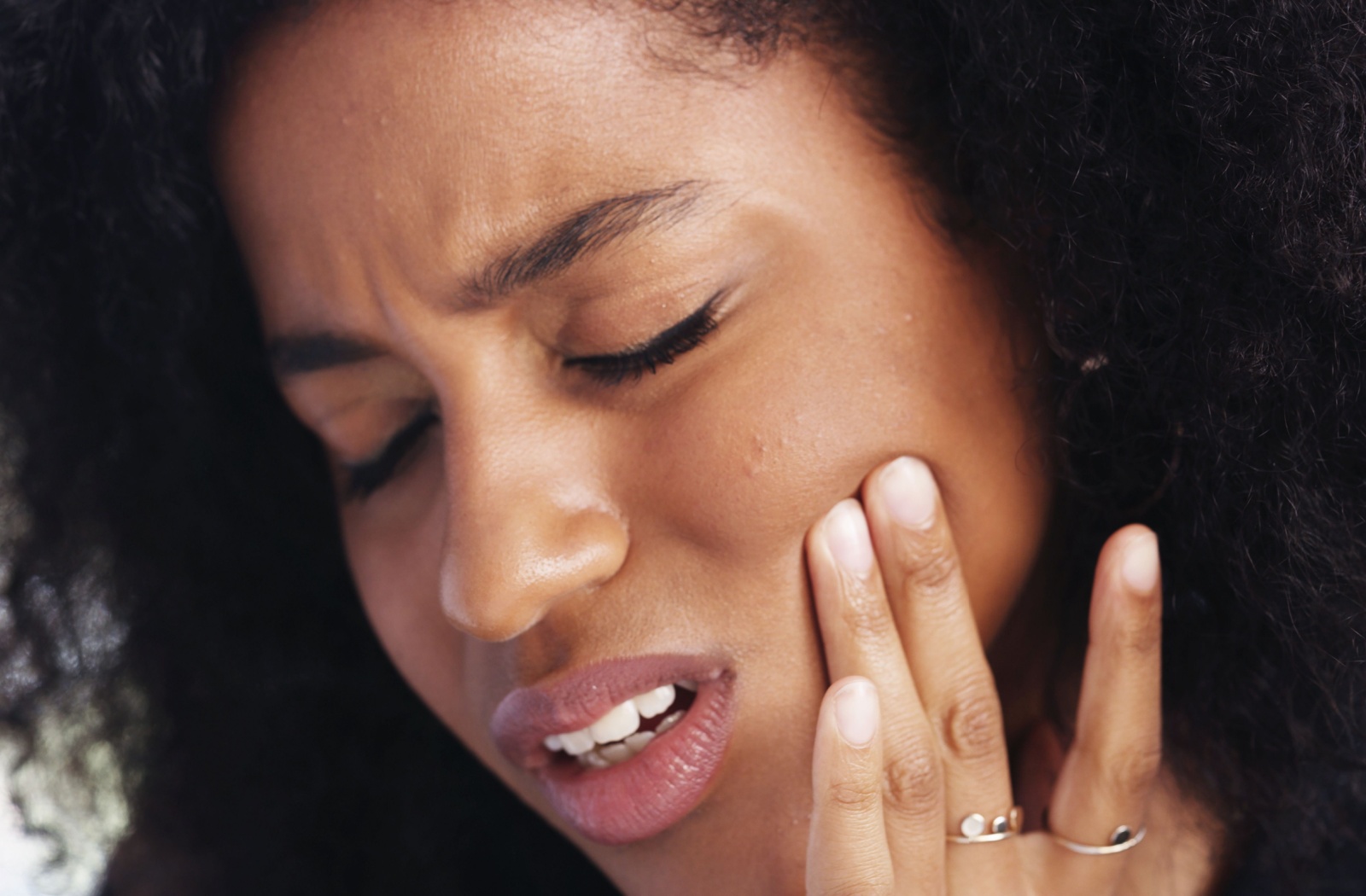 A person in discomfort, holding their jaw with two fingers as they experience pain due to TMJ disorder