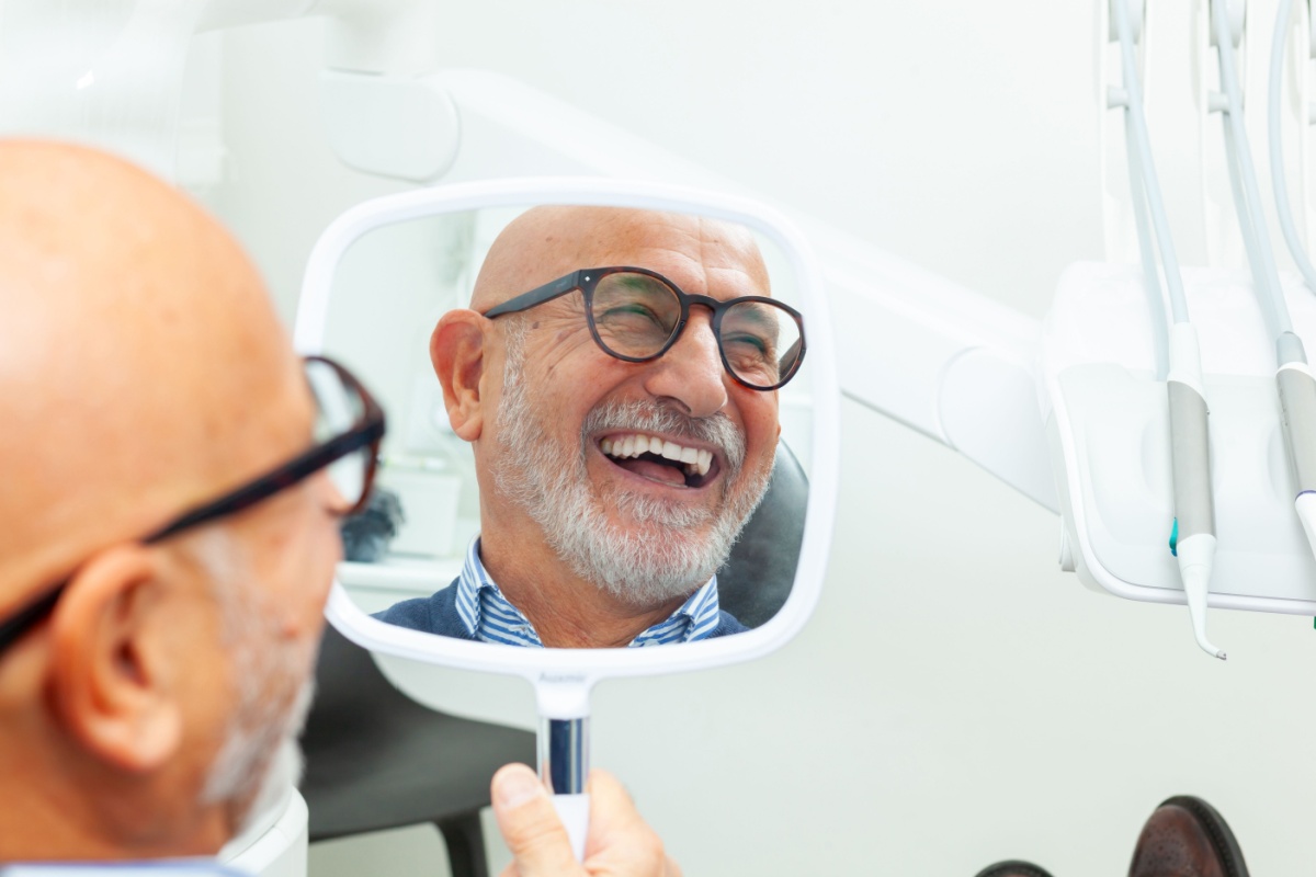 A dental patient smiling into a handheld mirror after getting dental implants.